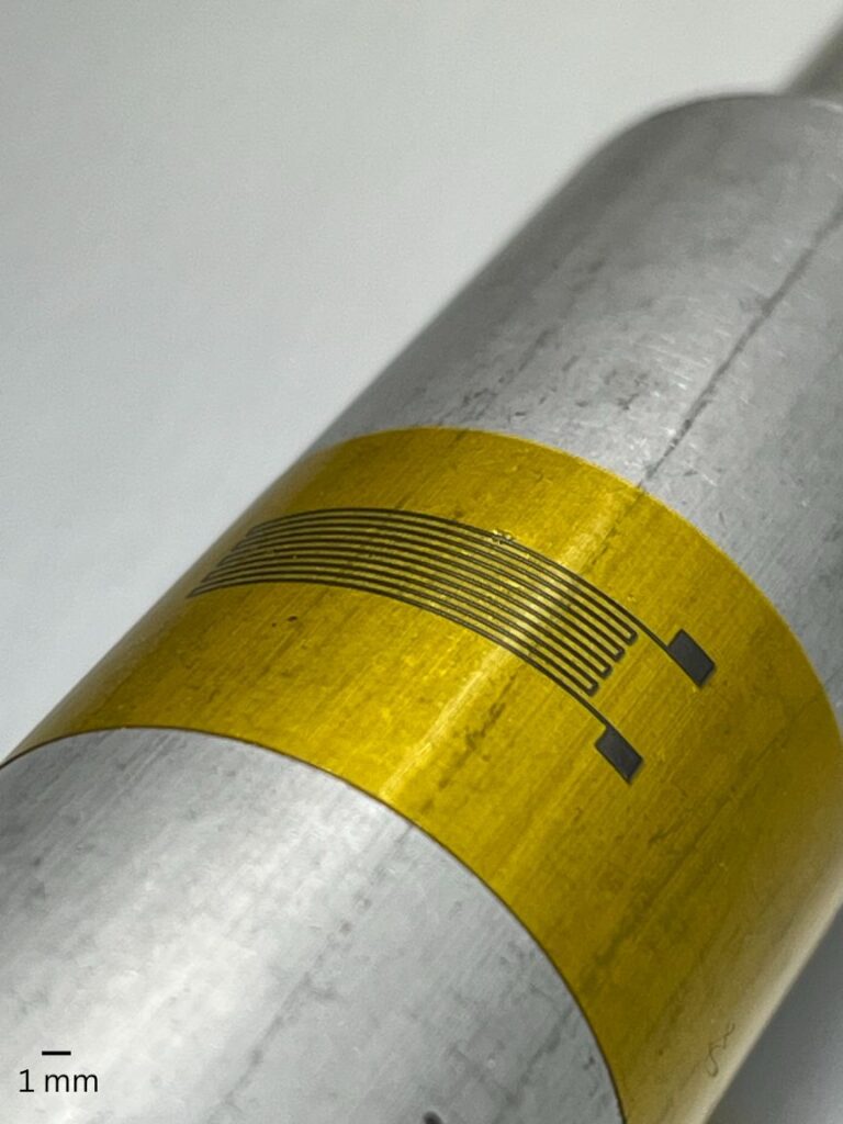 Close up picture of a platinum resistor / strain gauge that was NanoJet aerosol printed onto a curved polyimide and aluminum surface
