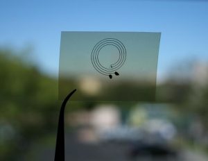 NanoJet printed double spiral on PET plastic that is held in tweezers and shown against a blurry background